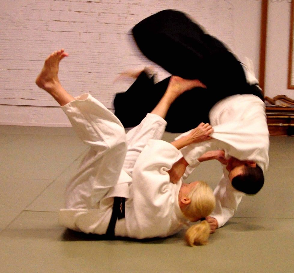 Jujutsu practice showing a throwing technique between two practitioners in white uniforms